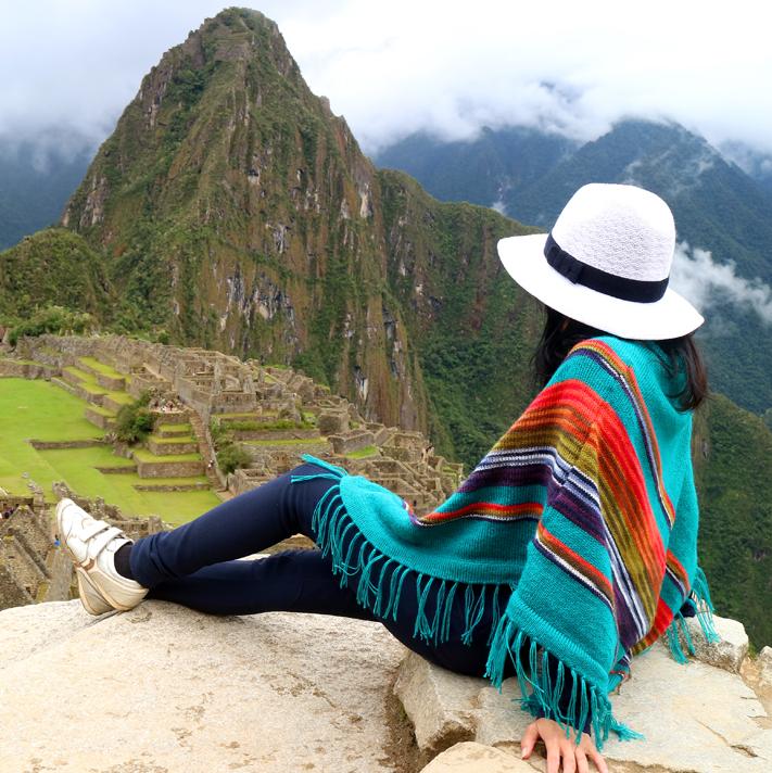 Woman sitting on a rock in a brightly colored poncho overlooking Machu Picchu